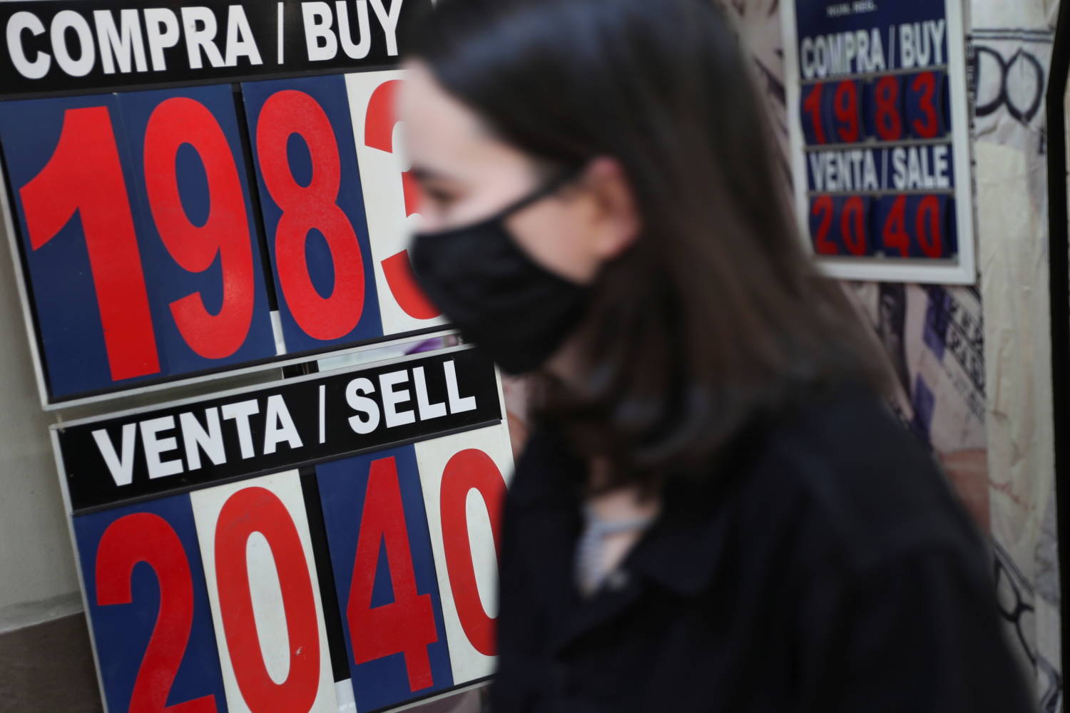 A Woman Walks Past A Board Displaying The Exchange Rate For Mexican Peso And U.s. Dollar At A Currency Exchange Shop In Downtown Mexico City