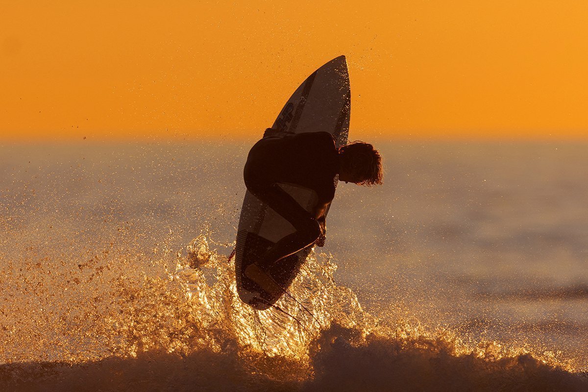 A Surfer Rides A Wave At Sunset In California