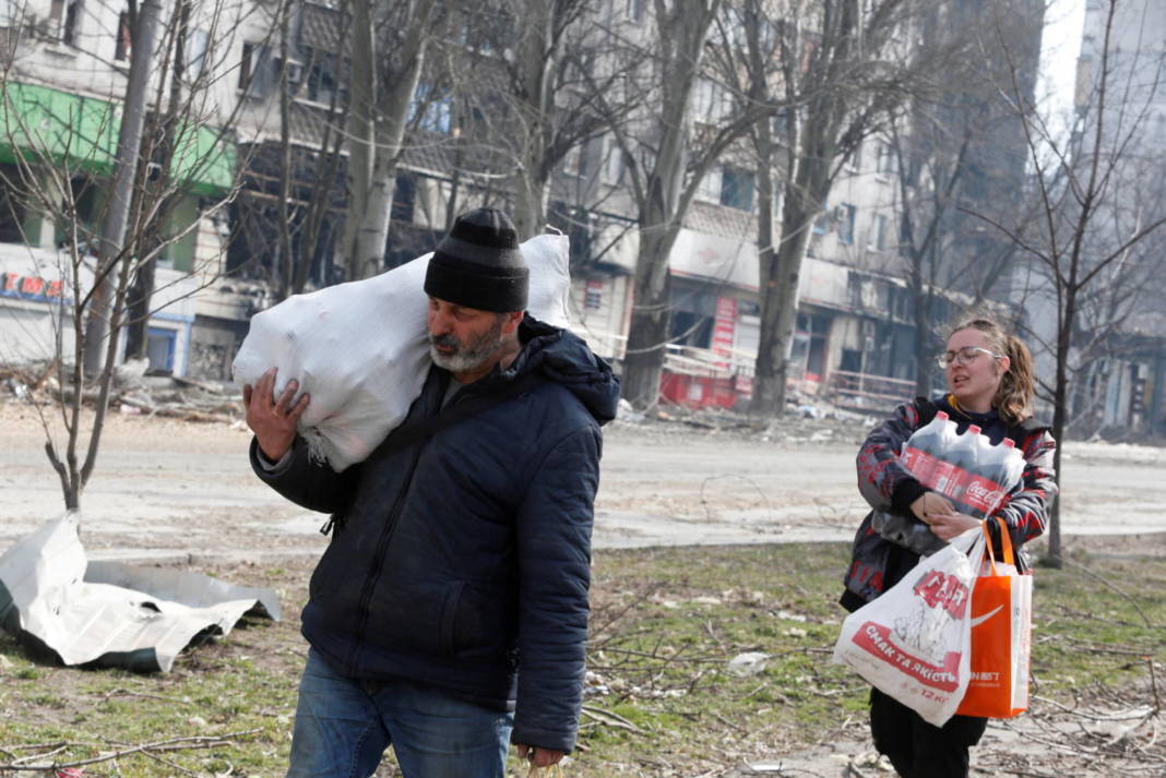 Local Residents Carry Foodstuff While Walking Past A Damaged Apartment Building In Mariupol
