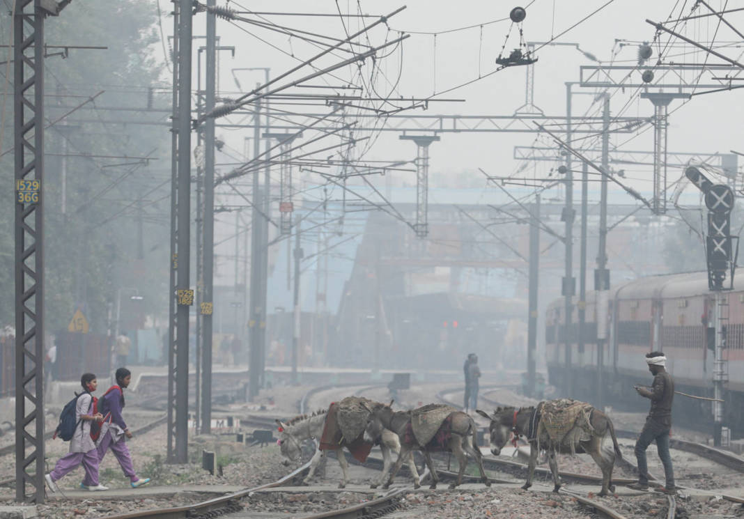 File Photo: School Girls And Mules Are Seen Crossing Railway Tracks On A Smoggy Morning In New Delhi