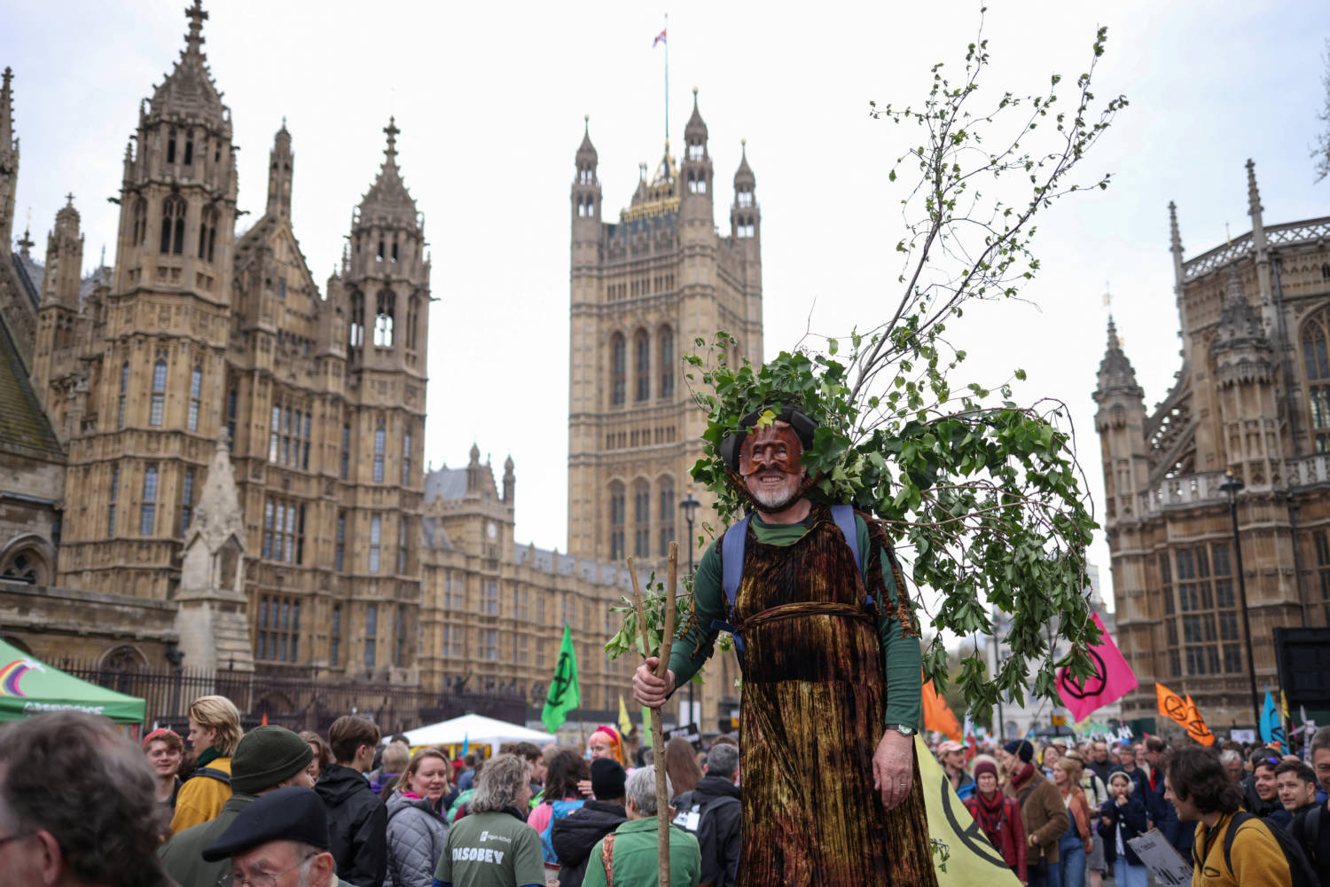 A Man Dressed As A Tree Walks Past The Houses Of Parliament