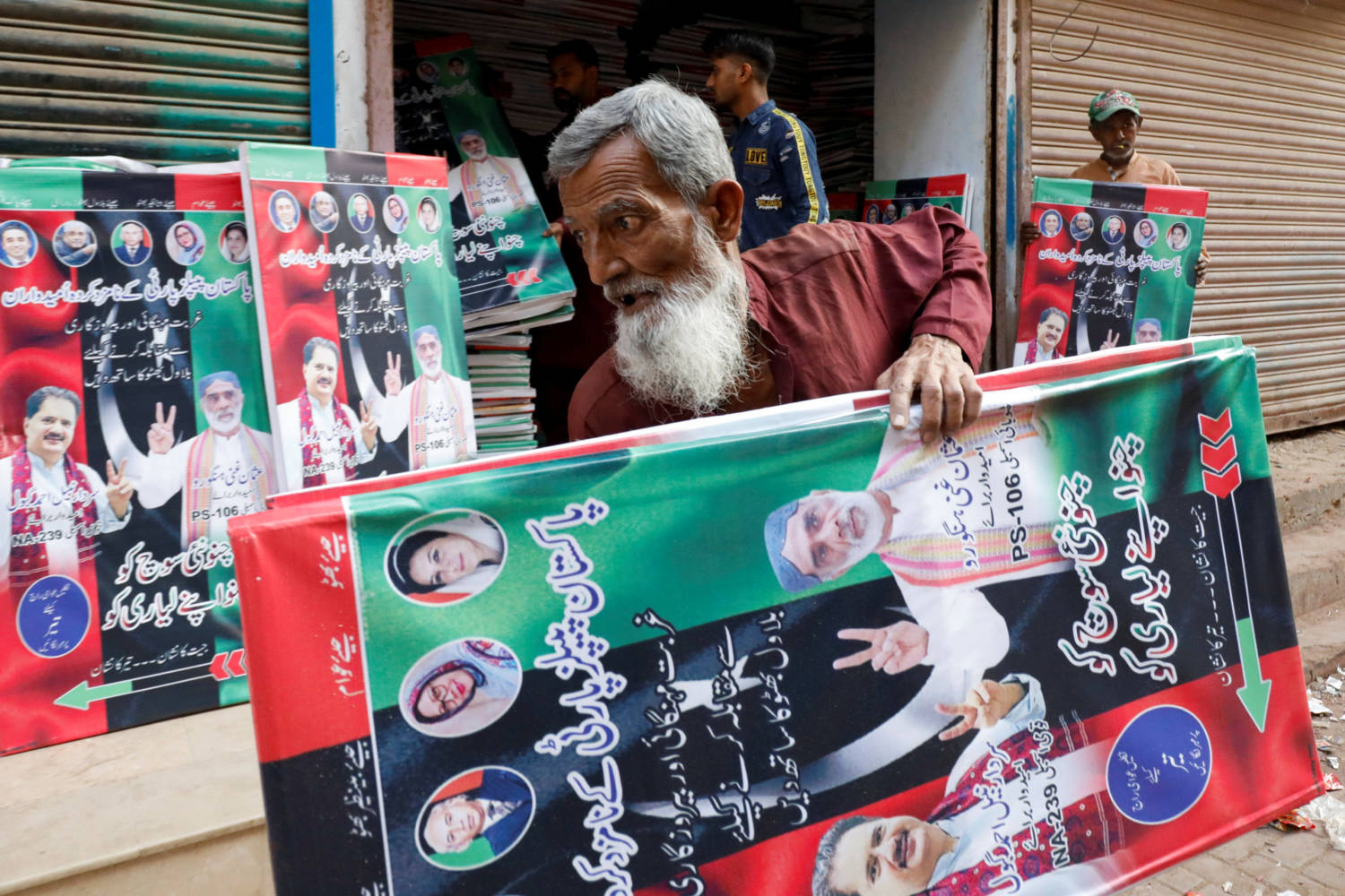 A Worker Carries Campaign Posters Of A Political Party To Decorate The Area, Ahead Of General Elections, In Karachi