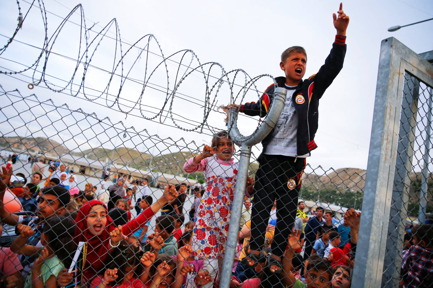File Photo: Refugee Youths Gesture From Behind A Fence As Officals Arrive At Nizip Refugee Camp Near Gaziantep