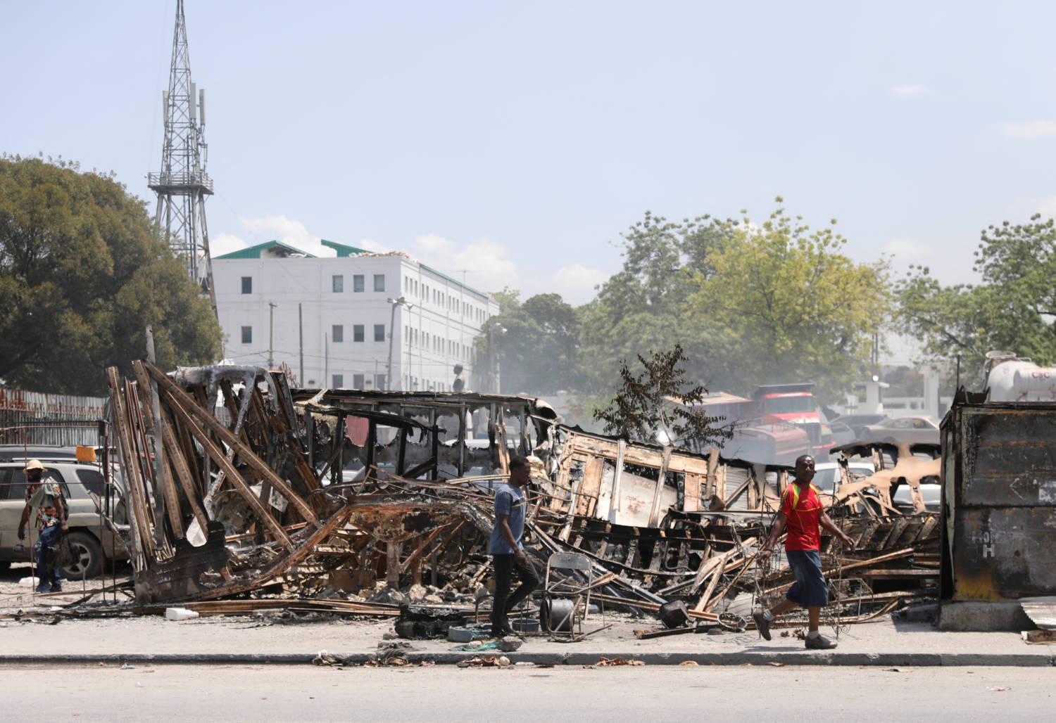 People Walk Past Remains Of Vehicles After They Were Set On Fire By Gangs, In Port Au Prince